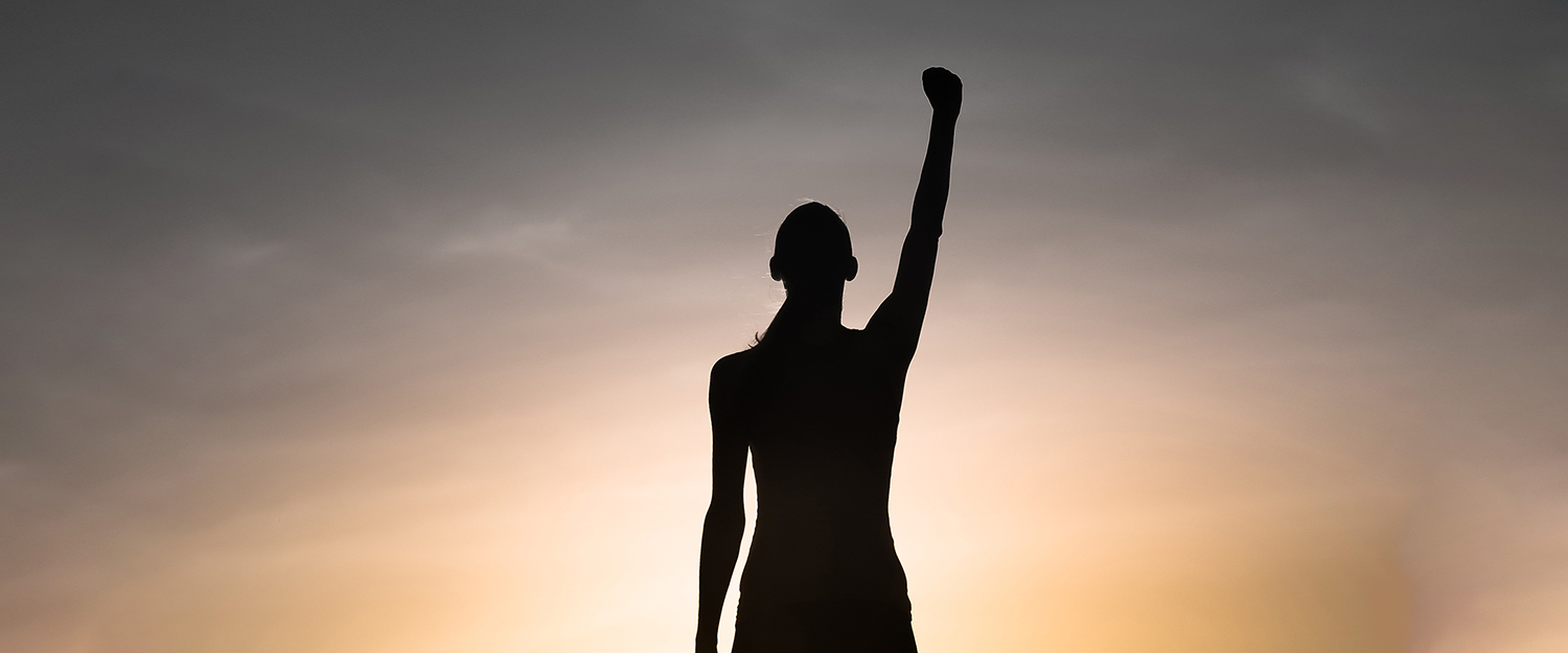 Mujer joven fuerte, victoriosa y motivada levantando el puño hacia el cielo del atardecer.